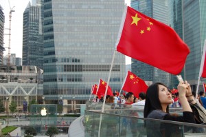 A young woman uses her iPhone to take a photo in Luijiazui, China with an Apple store visible in the background. China has become a vital market for Apple products.